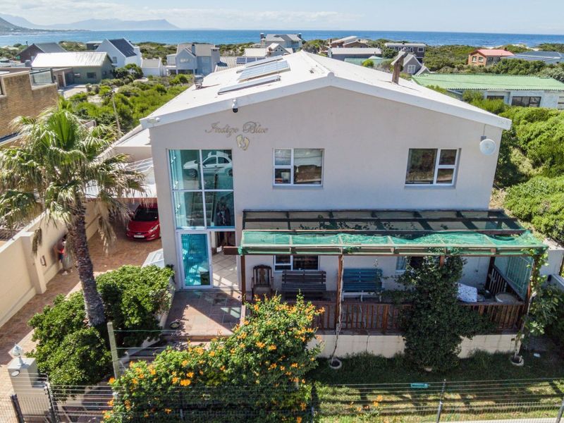 Aerial view of a coastal property featuring a metal roof with solar panels, a covered patio area, and secure perimeter electric fencing.