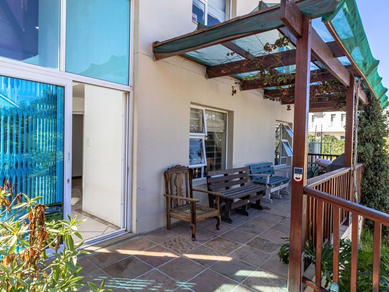 A covered patio area featuring tiled flooring, a timber pergola structure, and direct access to the interior through large sliding glass doors.