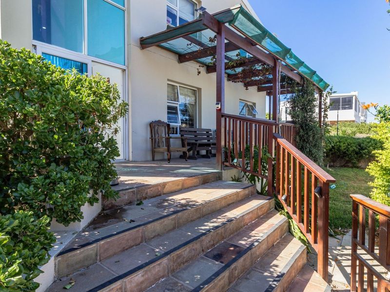 A raised patio area featuring a timber pergola, tiled steps with a wooden balustrade, and direct access to the home via sliding glass doors.