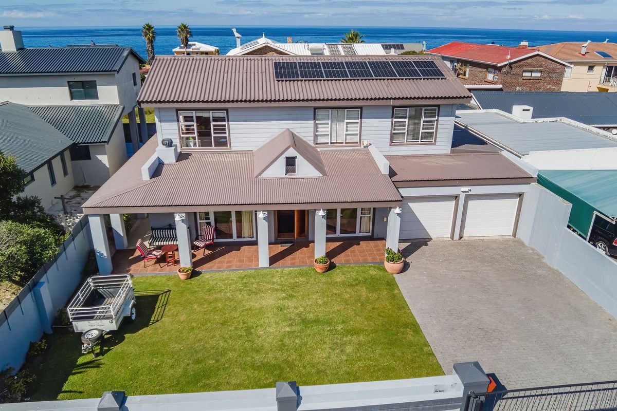 Aerial view of a two-story coastal home featuring a corrugated metal roof with solar panels, a covered patio, double garage, and a paved driveway.