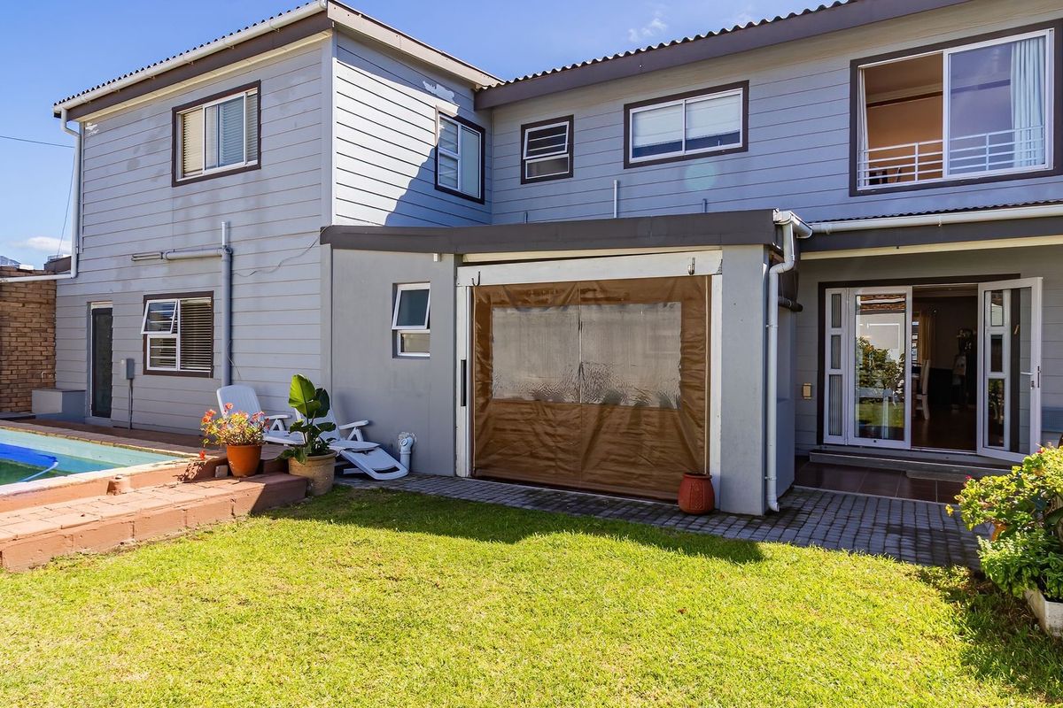 Rear view of the property featuring a swimming pool, paved patio area with protective blinds, and a well-maintained lawn.