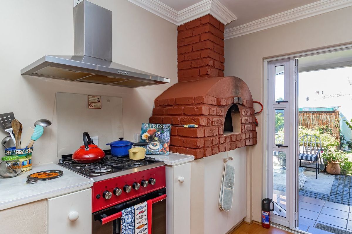 A functional kitchen featuring a gas stove with stainless steel extractor fan and a unique built-in brick pizza oven, with direct access to the patio.