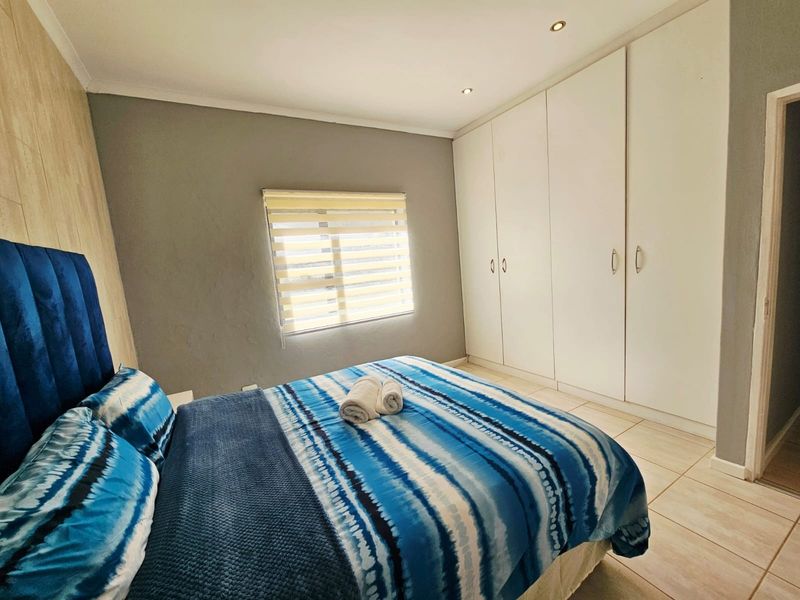 A well-maintained bedroom featuring neutral grey walls, tiled flooring, ample built-in cupboard storage, and modern recessed downlighting.