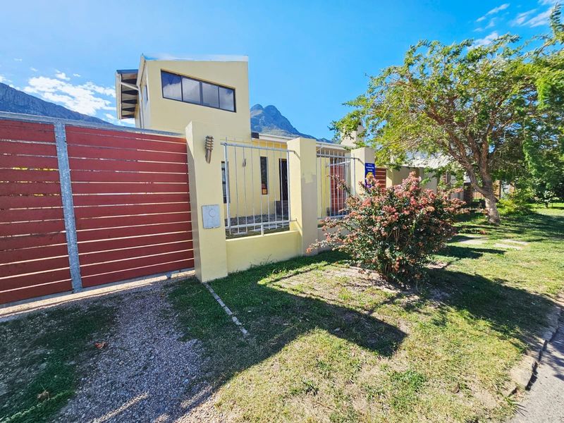 Front exterior view of the property featuring a gated entrance, perimeter wall with security fencing, and a driveway, set against a mountain backdrop.