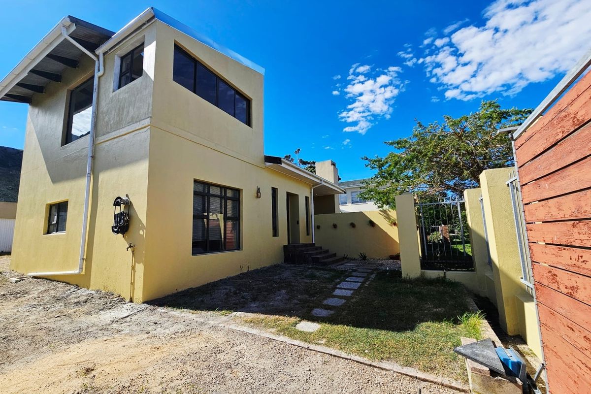 Rear exterior view of a two-story house featuring a paved walkway, stepped entrance, and boundary wall with metal security gate.