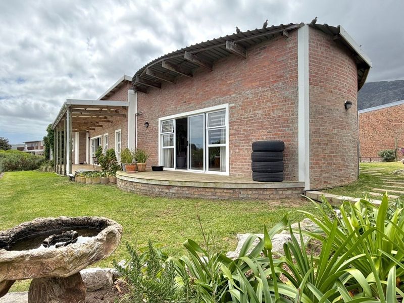 Rear view of a unique brick house featuring a curved roof design, a wooden deck, and a covered patio area overlooking the garden.