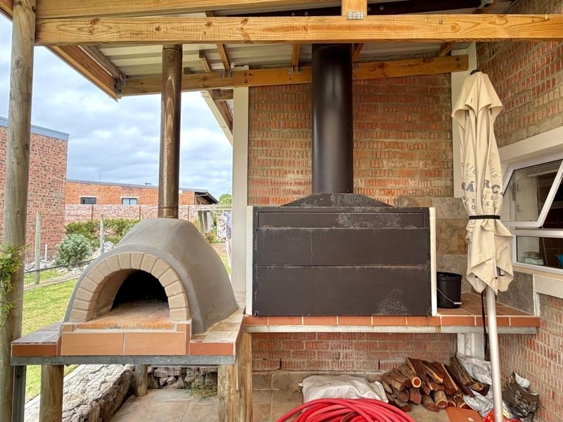Covered outdoor patio area featuring a built-in brick pizza oven and a large built-in braai, perfect for outdoor entertaining.