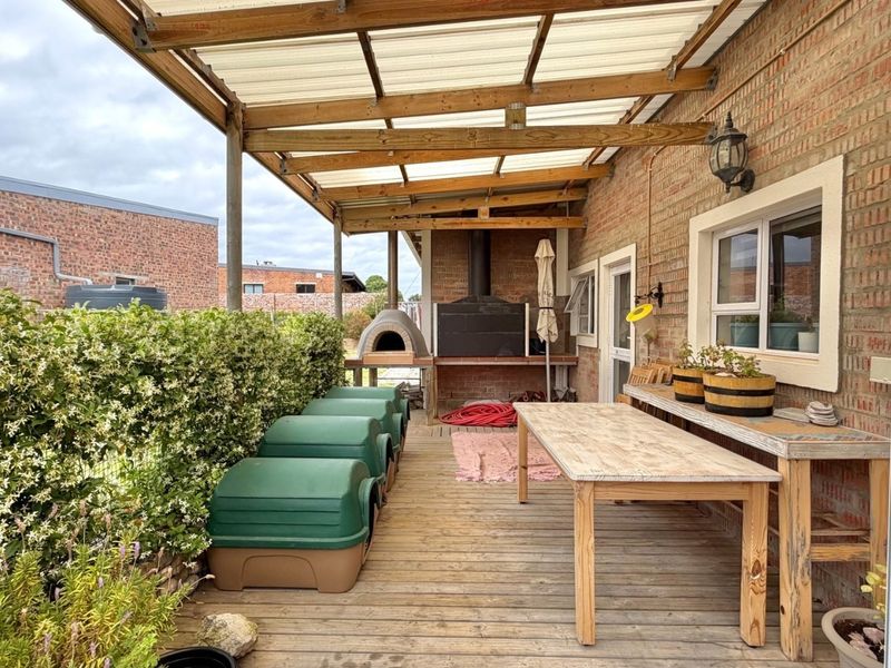 Covered outdoor patio featuring timber decking, a built-in brick pizza oven, and a brick braai area, ideal for outdoor entertaining.