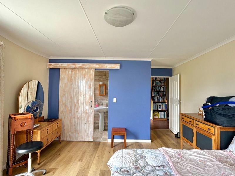 A well-maintained bedroom featuring laminate flooring, a sliding barn door leading to an en-suite bathroom, and neutral wall finishes.