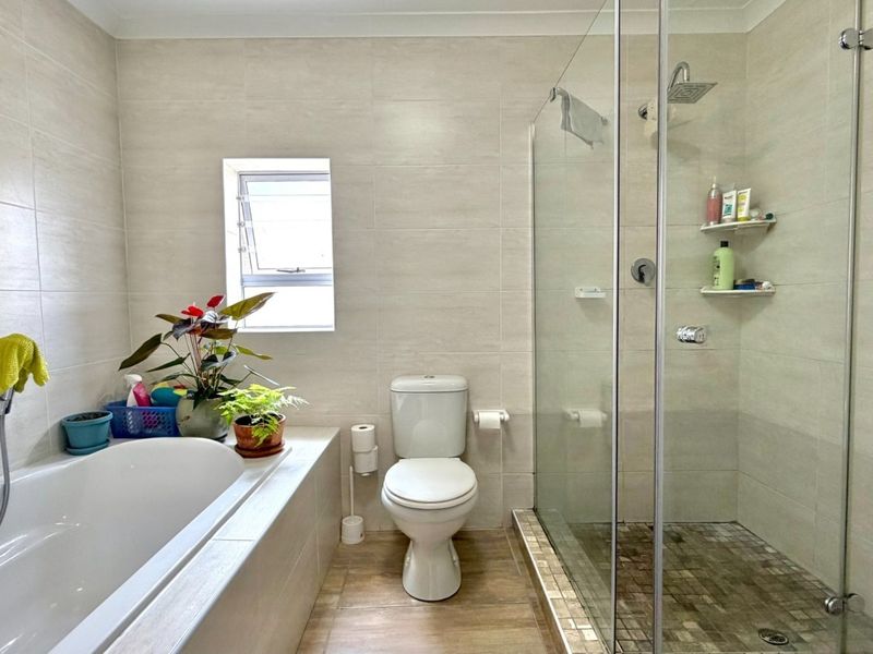 Modern bathroom featuring a built-in bathtub, separate glass-enclosed shower, and neutral wall tiling, providing a clean and functional space.