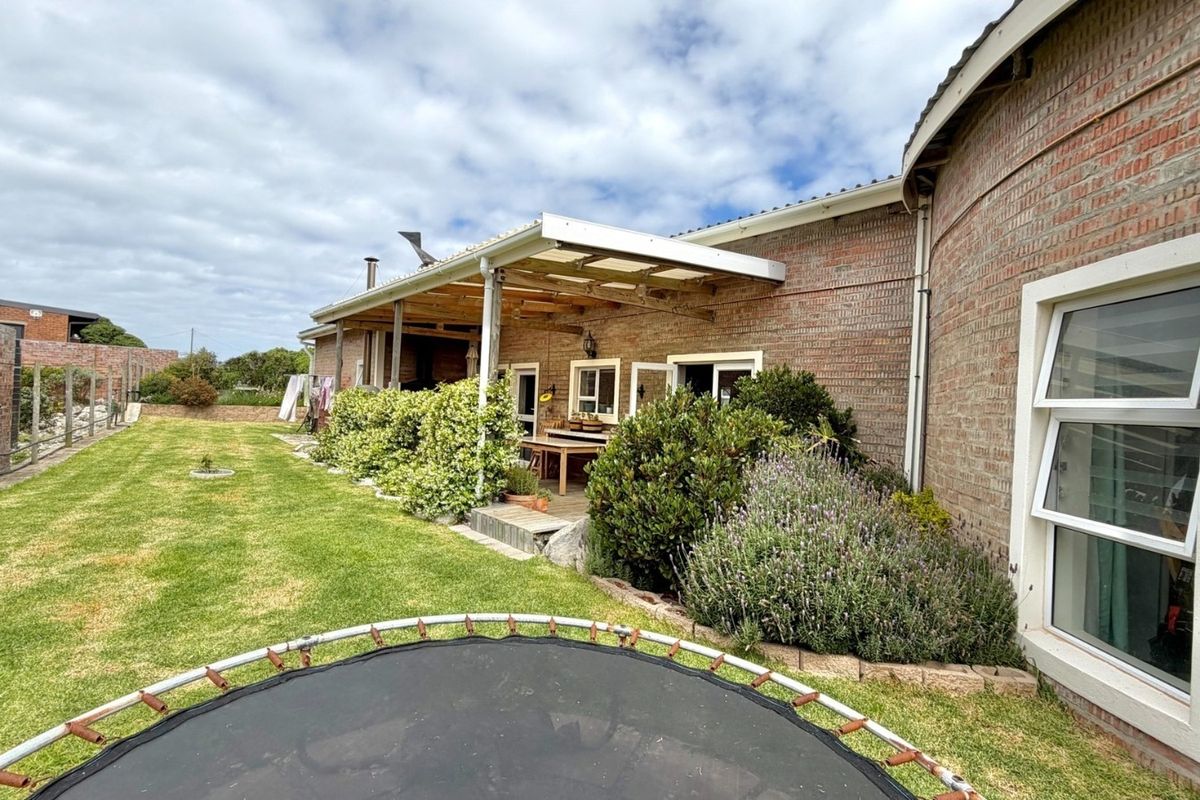 Rear view of the property featuring a brick facade, a covered patio area with timber decking, and a well-maintained garden lawn.