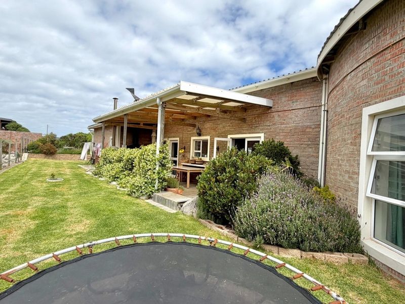 Rear view of the property featuring a brick facade, a covered patio area with timber decking, and a well-maintained garden lawn.