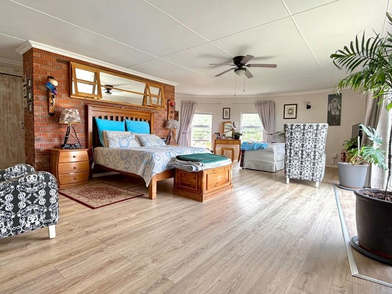 Spacious bedroom featuring exposed brick wall detailing, laminate flooring, a ceiling fan, and direct access to the outdoors via a sliding glass door.