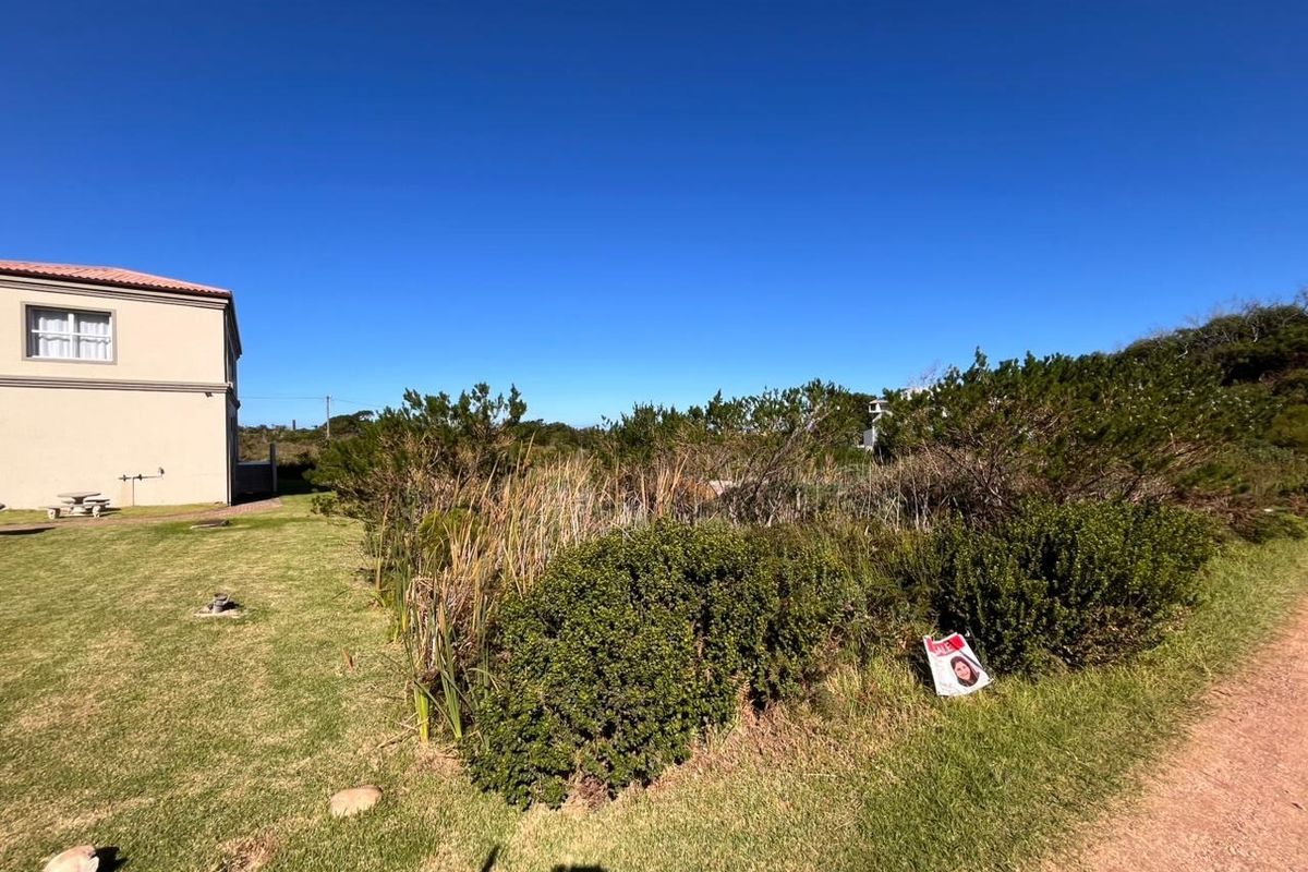 A view of a vacant residential plot featuring established lawn and native vegetation, adjacent to an existing residential structure.