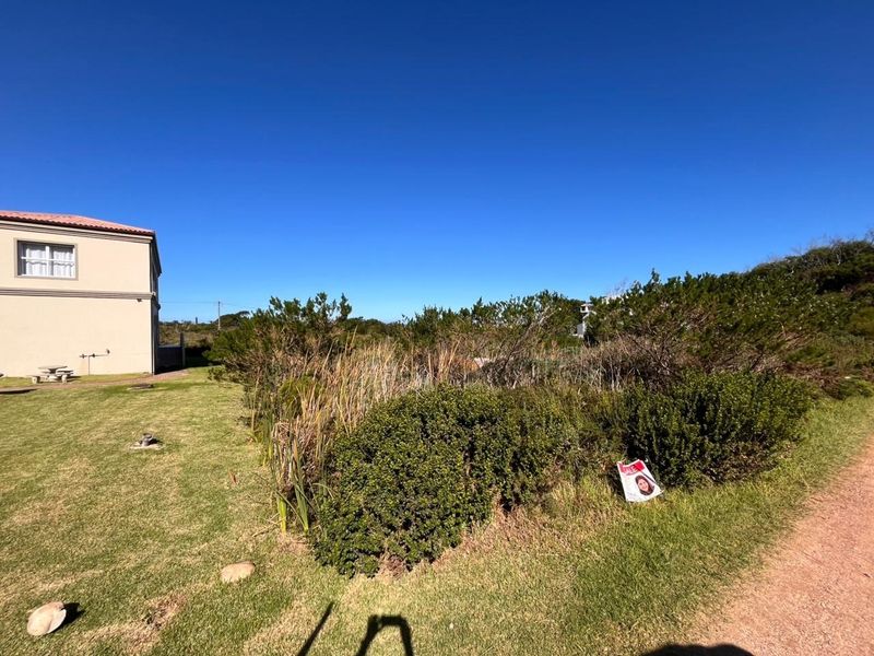 A view of a vacant residential plot featuring established lawn and native vegetation, adjacent to an existing residential structure.