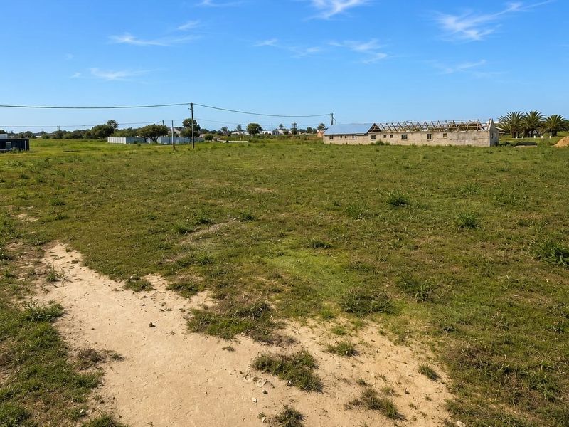 A wide-angle view of a vacant residential plot featuring open grassland, boundary fencing, and nearby utility infrastructure.