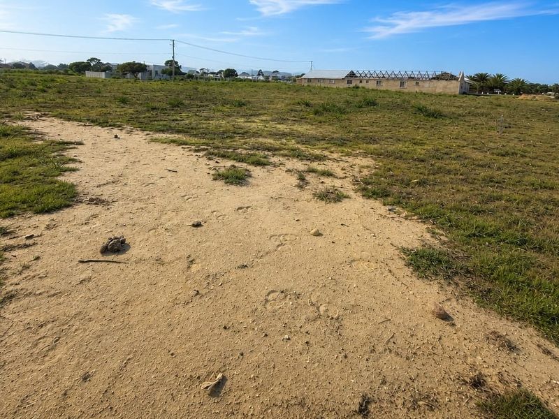 A wide-angle view of a vacant residential plot featuring natural grassland and a sandy pathway, offering a blank canvas for development.