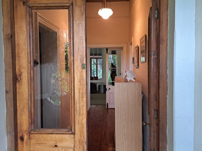 A traditional farmhouse entry featuring original timber doors, warm wood flooring, and a classic pendant light fixture leading into the home's interior.