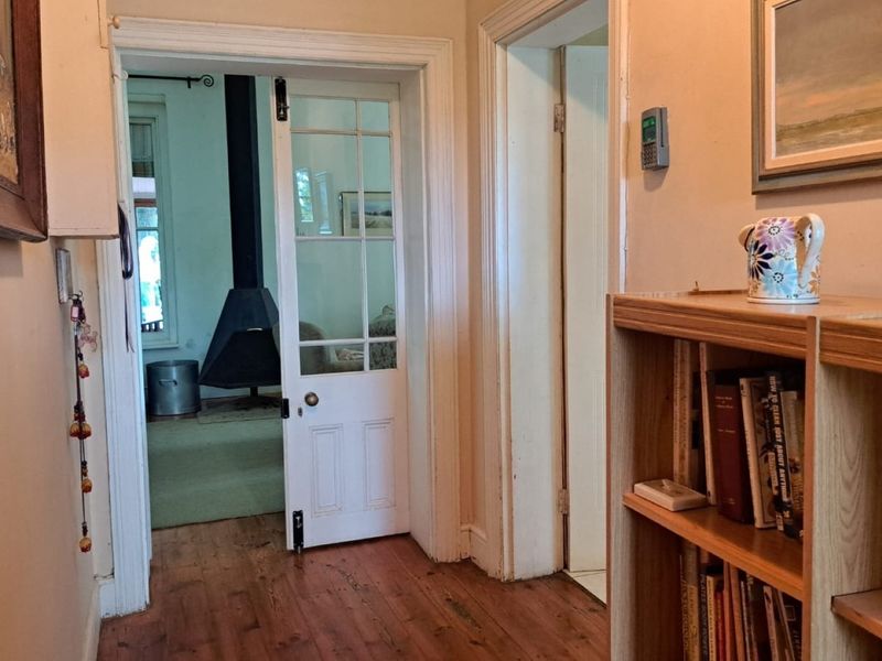 A hallway featuring hardwood flooring and a glass-paneled door leading to a living area with a freestanding fireplace.