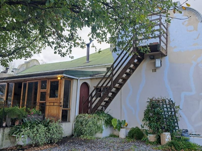 Rear elevation of a farm-style building featuring a timber-framed glass sunroom, an external staircase, and a corrugated metal roof.
