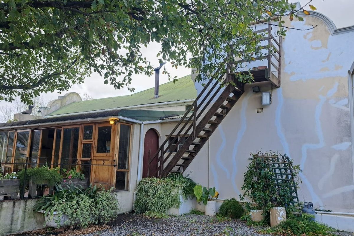 Rear elevation of a farm-style building featuring a timber-framed glass sunroom, an external staircase, and a corrugated metal roof.