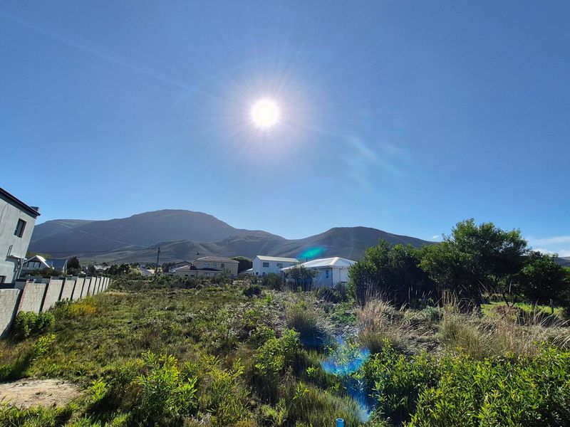 A view of a vacant residential plot featuring natural vegetation, a boundary wall, and scenic mountain views in the background.