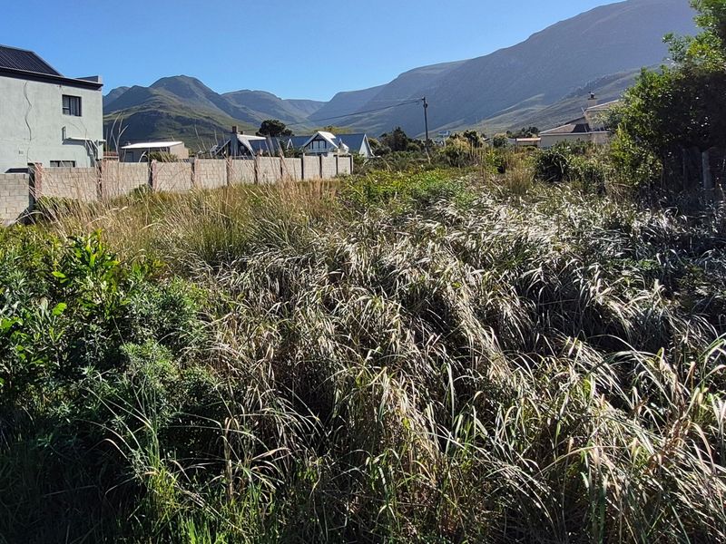 A vacant residential plot featuring overgrown vegetation, enclosed by boundary walls and fencing, with scenic mountain views in the background.