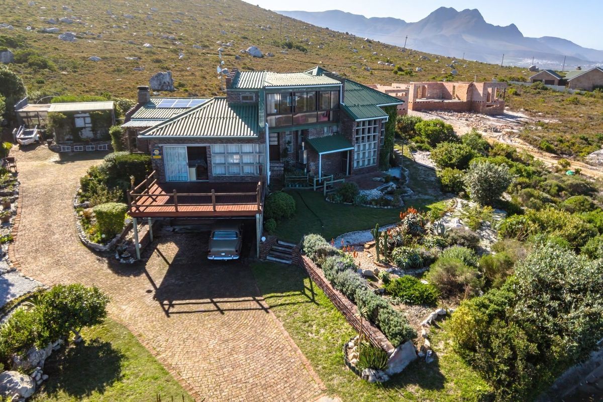 Aerial view of a multi-level brick residence featuring a metal roof, raised timber deck, and extensive landscaped grounds in a scenic coastal setting.