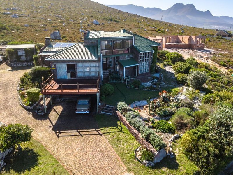 Aerial view of a multi-level brick residence featuring a metal roof, raised timber deck, and extensive landscaped grounds in a scenic coastal setting.