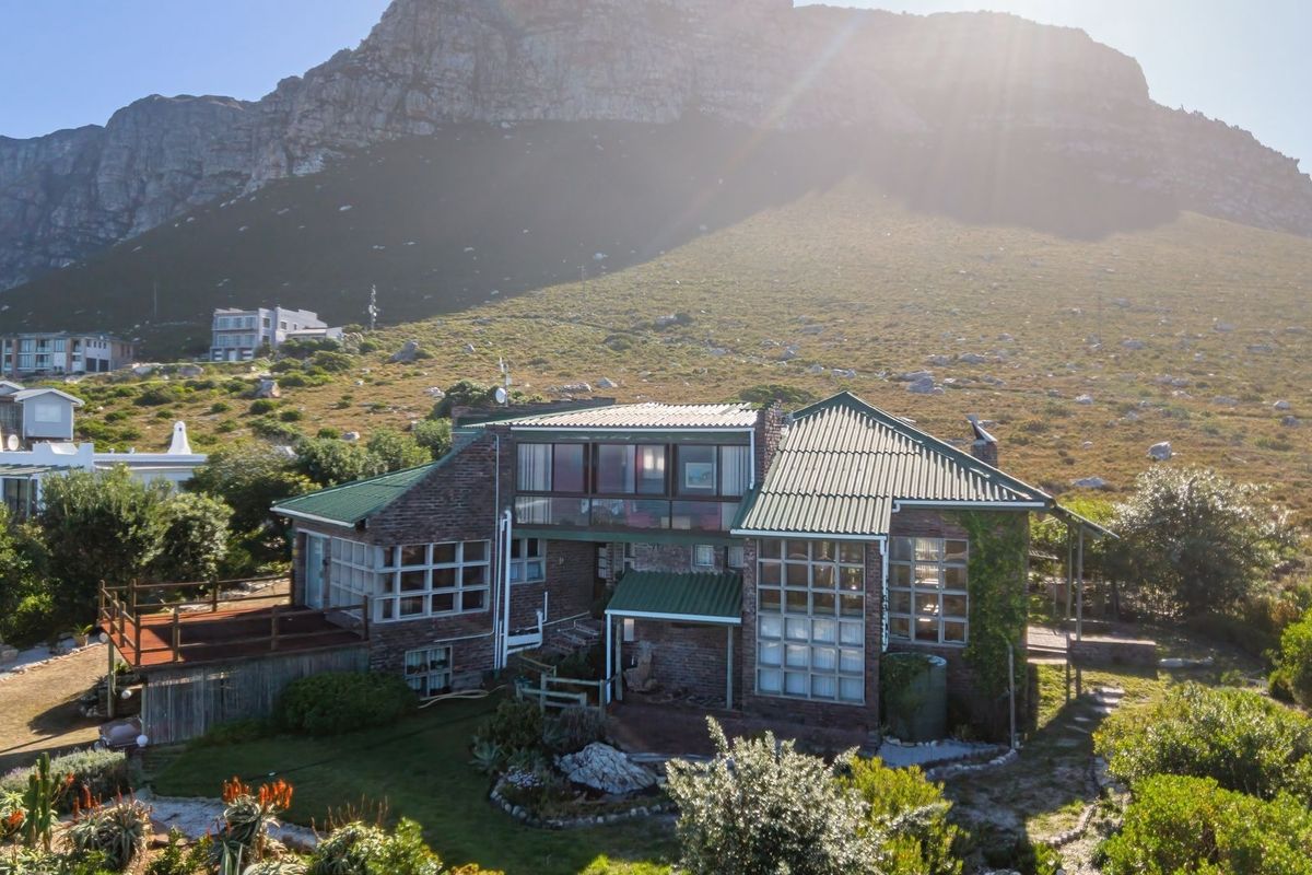 An elevated view of a brick-clad residence featuring a corrugated metal roof, large windows, and a timber deck, set against a mountain backdrop.