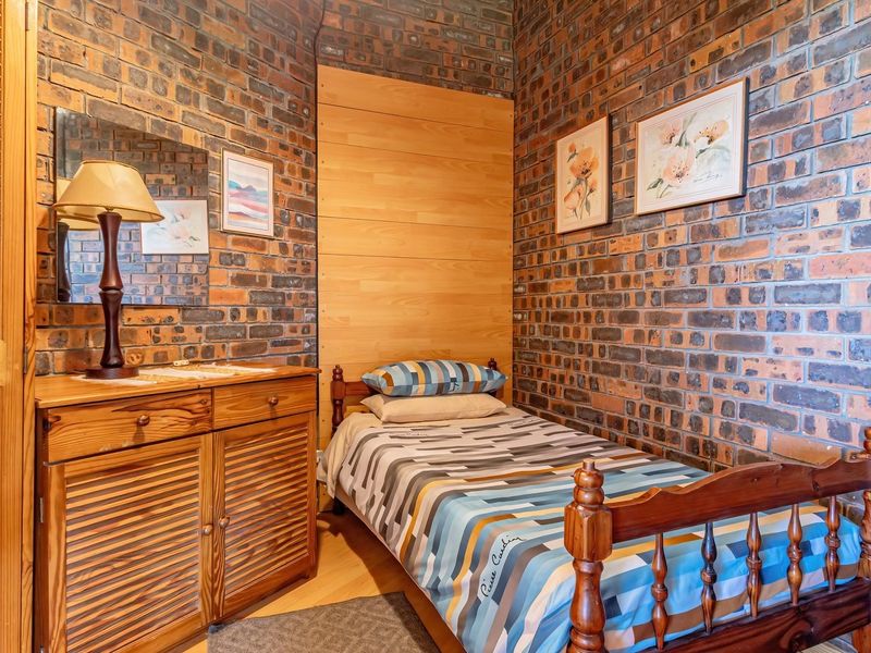 A cozy bedroom featuring distinctive exposed brick walls, wood paneling accents, and a built-in wooden closet for storage.