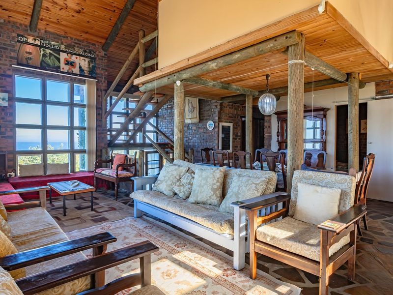 Spacious open-plan living and dining area featuring exposed brick walls, timber ceiling beams, a wooden staircase, and large windows with natural light.