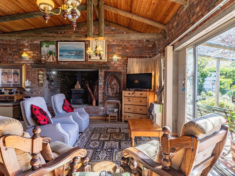 A rustic living room featuring exposed brick walls, a timber beam ceiling, and a wood-burning fireplace, with large sliding doors opening to the garden.