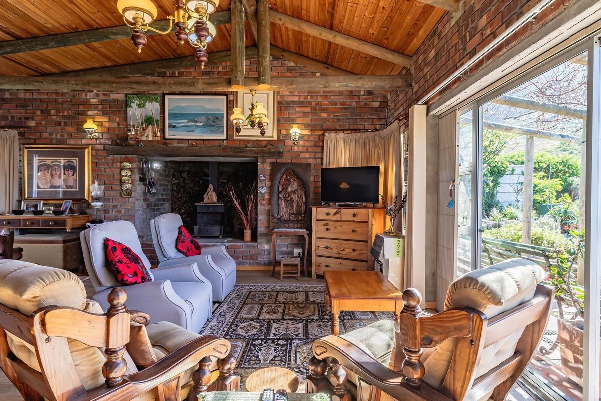A rustic living room featuring exposed brick walls, a timber beam ceiling, and a wood-burning fireplace, with large sliding doors opening to the garden.