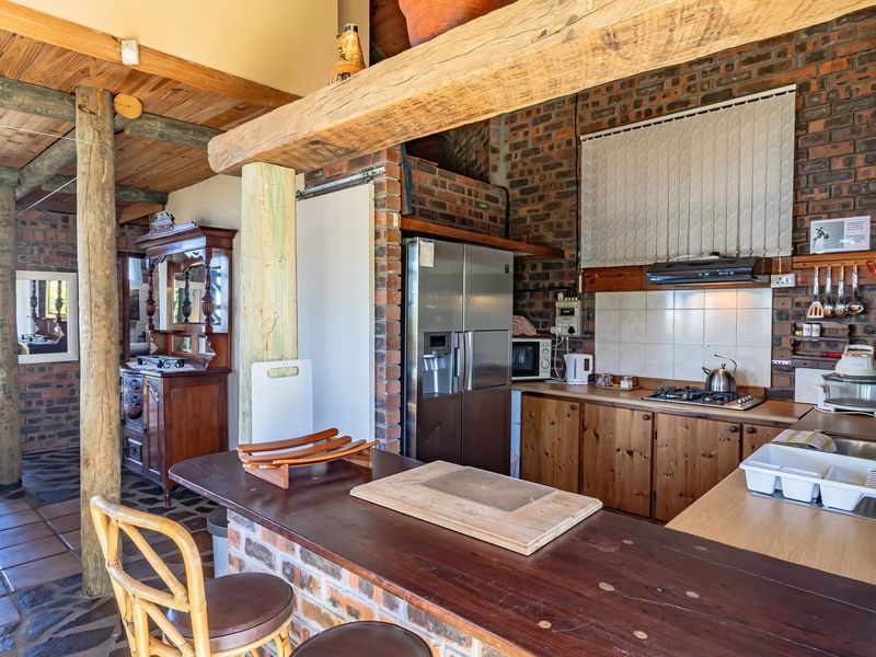 Open-plan kitchen and dining area featuring rustic exposed brick walls, timber ceiling beams, wooden cabinetry, and a breakfast bar with slate flooring.
