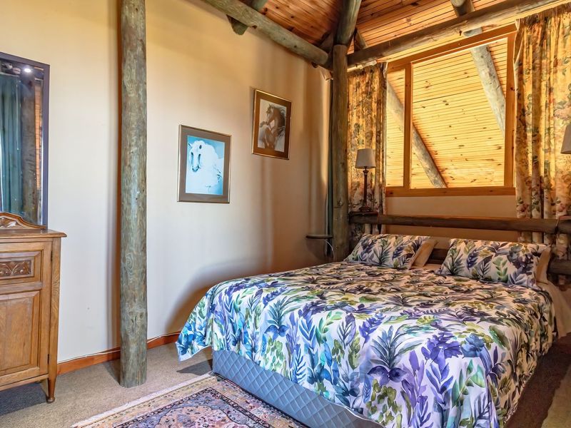 A rustic bedroom featuring exposed timber ceiling beams, wooden support posts, and a vaulted tongue and groove timber ceiling.