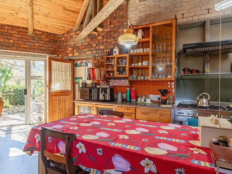 Rustic kitchen featuring exposed brick walls, timber vaulted ceilings, and built-in wooden cabinetry, with direct access to an outdoor patio area.