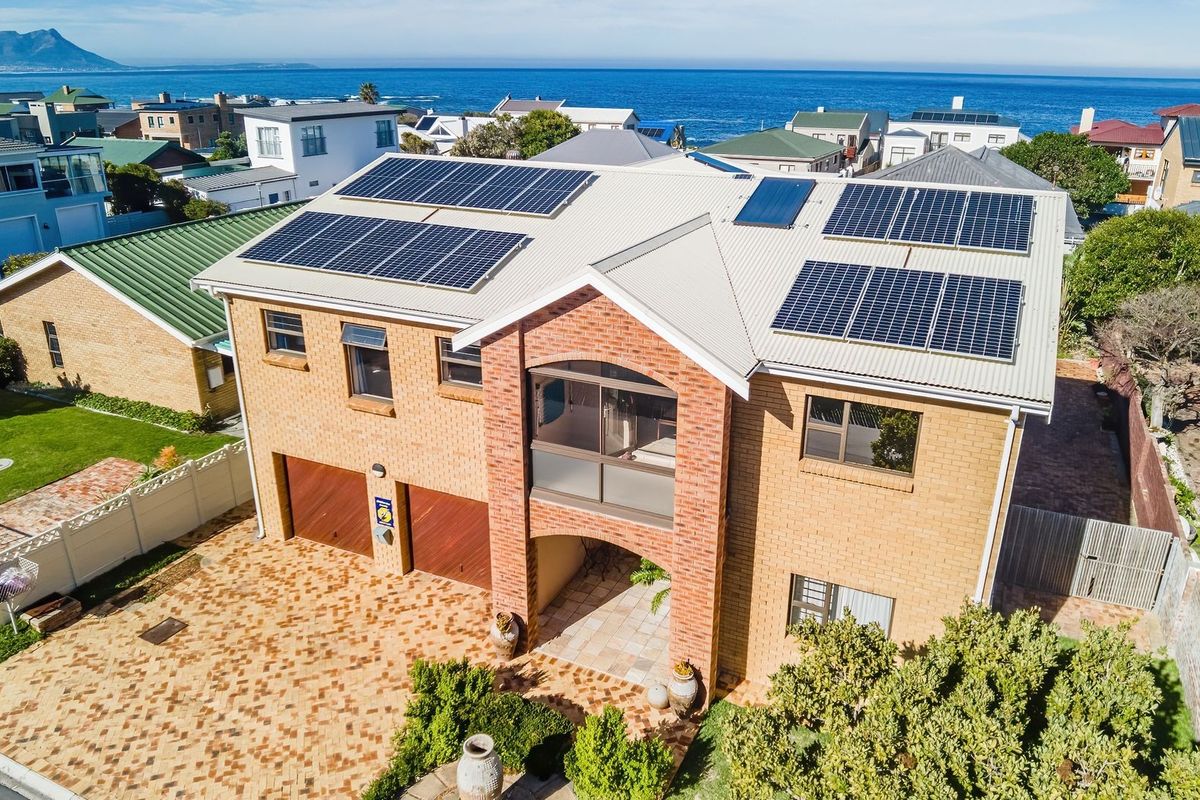 Aerial view of a double-story brick house featuring a metal roof with extensive solar panel installation, a paved driveway, and a double garage.