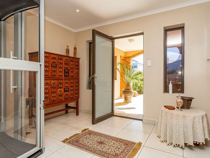 Bright and welcoming entrance hall featuring tiled flooring, a modern glass door, and a decorative brick feature wall leading to an outdoor patio area.