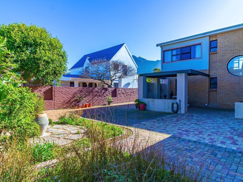 Rear exterior view featuring a paved courtyard, a covered patio structure, and a brick boundary wall with established garden landscaping.