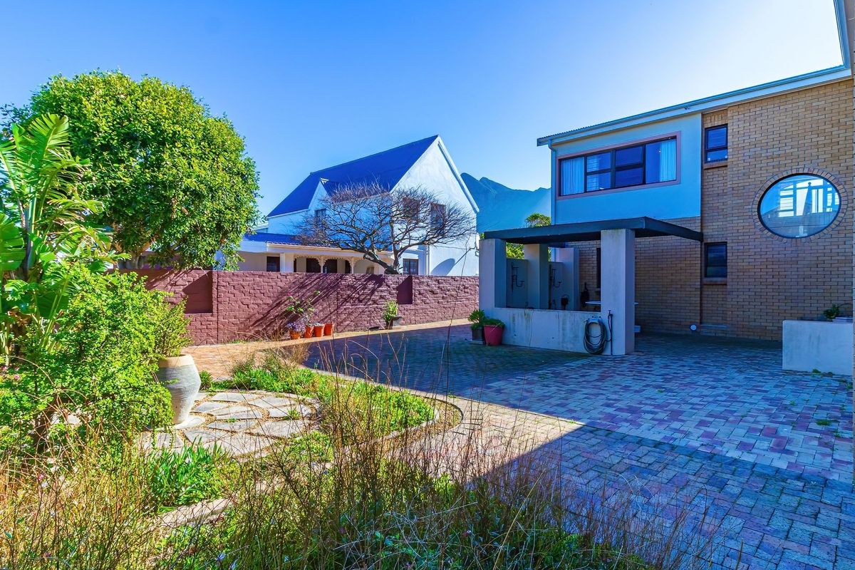 Rear exterior view featuring a paved courtyard, a covered patio structure, and a brick boundary wall with established garden landscaping.