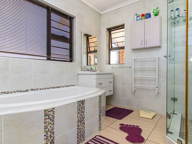 A well-maintained bathroom featuring a built-in bathtub with mosaic tile accents, a separate glass shower enclosure, vanity cabinet, and a wall-mounted towel warmer.