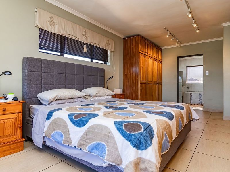 Spacious bedroom featuring extensive built-in wooden cabinetry, tiled flooring, modern track lighting, and direct access to an en-suite bathroom.