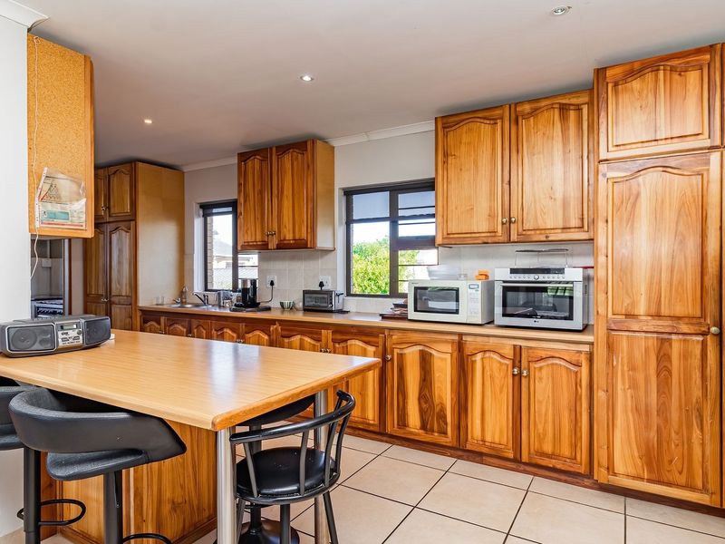 A functional kitchen featuring extensive wooden cabinetry, tiled flooring, and a built-in breakfast counter, offering ample storage and workspace.