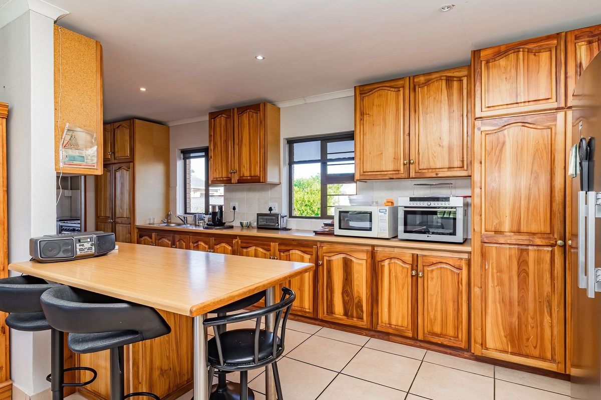 A functional kitchen featuring extensive wooden cabinetry, tiled flooring, and a built-in breakfast counter, offering ample storage and workspace.