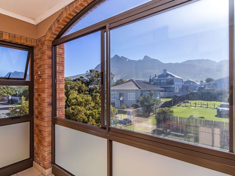A sunroom or enclosed balcony featuring exposed brick walls, large arched windows, and expansive mountain views.
