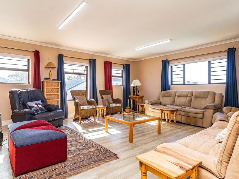 Spacious living room featuring light-toned laminate flooring, multiple aluminium-framed windows, and functional strip lighting, offering a bright and comfortable family area.