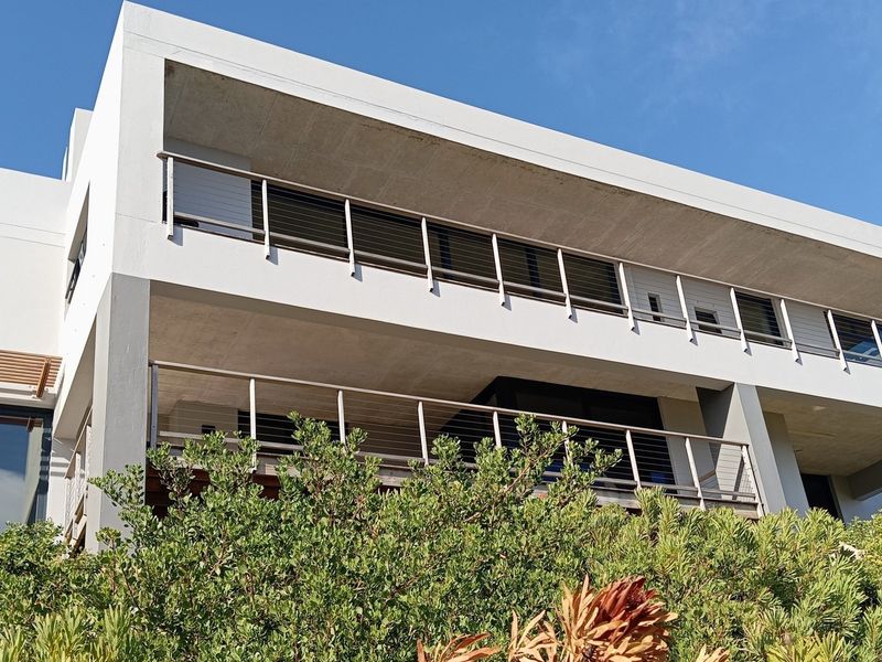 Modern multi-story residential exterior featuring expansive concrete balconies with stainless steel cable railings and large glass sliding doors.