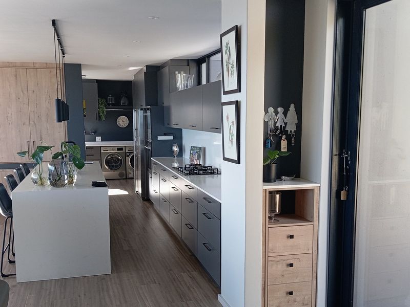 Modern open-plan kitchen featuring sleek dark cabinetry, a central stone island, integrated appliances, and high-quality finishes throughout.