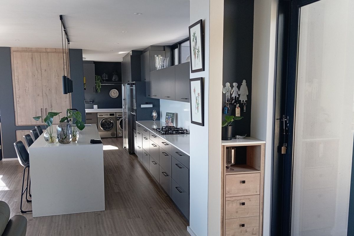Modern open-plan kitchen featuring sleek dark cabinetry, a central stone island, integrated appliances, and high-quality finishes throughout.